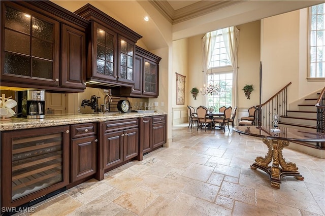 bar with stone tile floors, ornamental molding, a high ceiling, stairs, and wine cooler