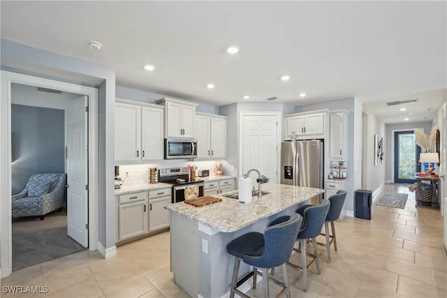 847 Stonewater Lake Ter, Cape Coral, FL 33993 - kitchen with stainless steel appliances, a sink, a breakfast bar, a kitchen island with sink, and light stone counters