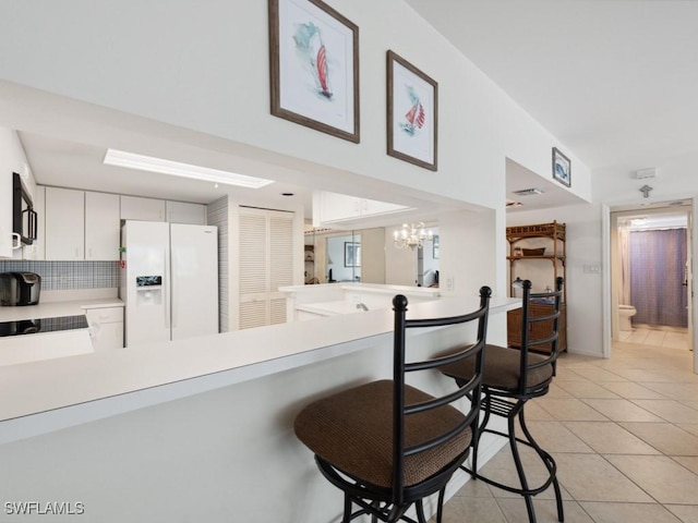 kitchen featuring light tile patterned floors, light countertops, a peninsula, white refrigerator with ice dispenser, and a breakfast bar area
