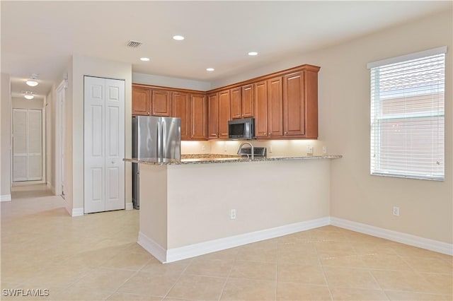 10486 Winged Elm Ln, Fort Myers, FL 33913 - kitchen with light stone counters, light tile patterned floors, a peninsula, brown cabinetry, and freestanding refrigerator