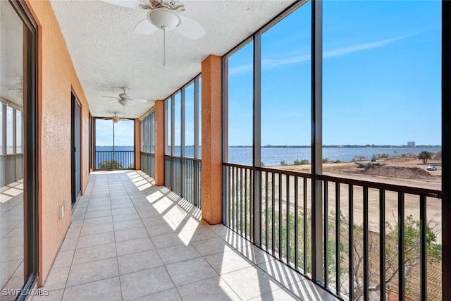 unfurnished sunroom featuring a ceiling fan, a water view, and a wealth of natural light