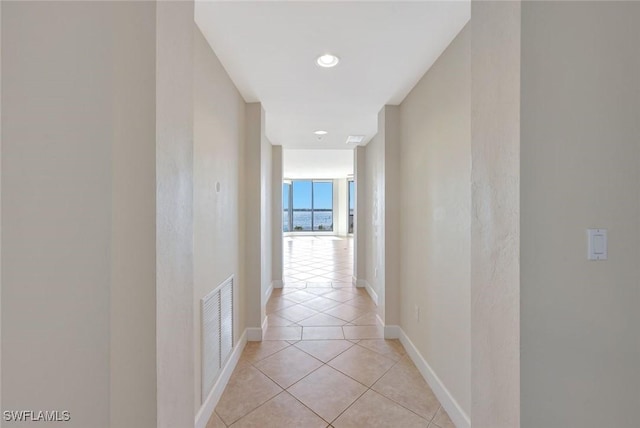 corridor featuring baseboards, visible vents, and light tile patterned floors