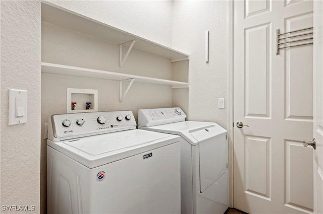 clothes washing area with a textured wall, washer and dryer, and laundry area