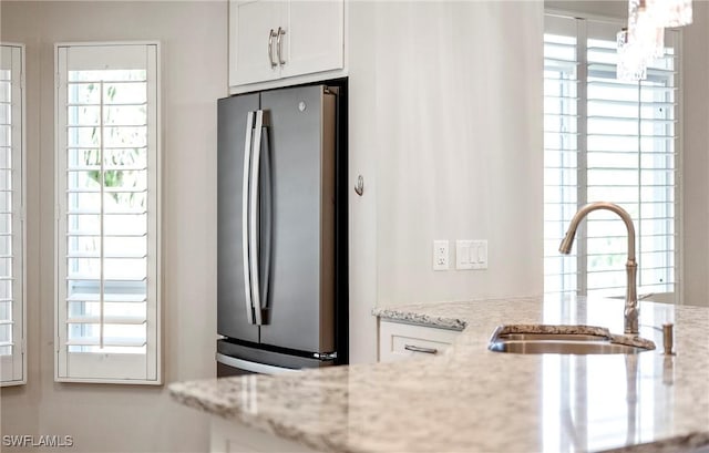 kitchen with white cabinets, a sink, freestanding refrigerator, an inviting chandelier, and light stone counters