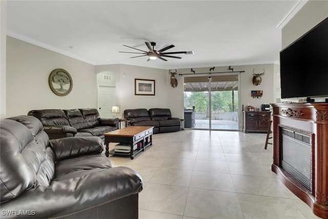living room featuring ceiling fan, crown molding, light tile patterned flooring, and a glass covered fireplace