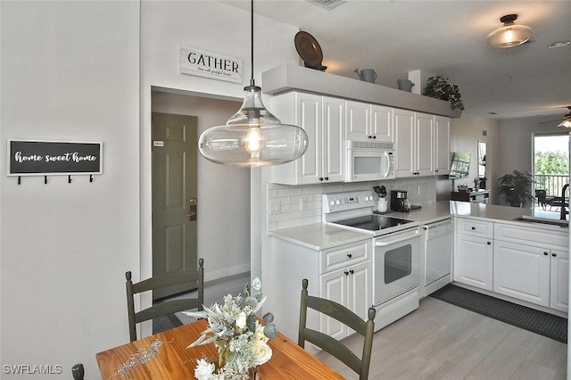 kitchen with a sink, light countertops, white appliances, light wood finished floors, and decorative backsplash
