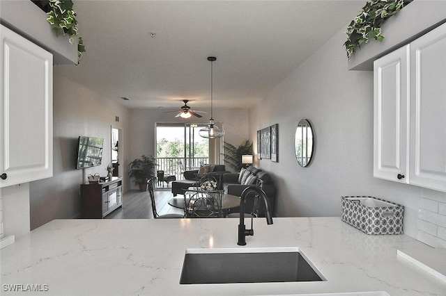 kitchen featuring open floor plan, white cabinetry, a ceiling fan, light stone countertops, and a sink