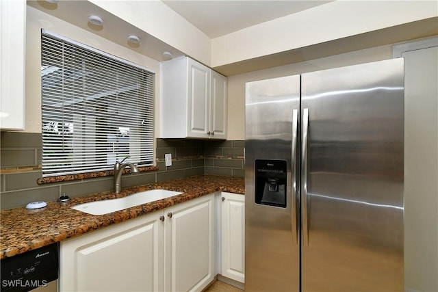 kitchen with a sink, dark stone counters, decorative backsplash, stainless steel refrigerator with ice dispenser, and white cabinetry
