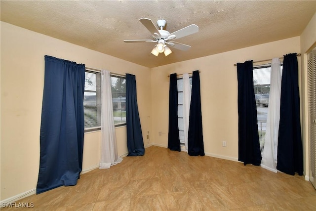empty room featuring plenty of natural light, a ceiling fan, baseboards, and a textured ceiling