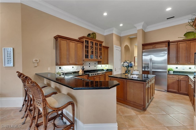 1716 Venezia Way, Naples, FL 34105 - kitchen with stainless steel appliances, brown cabinetry, a center island, tasteful backsplash, and ornamental molding