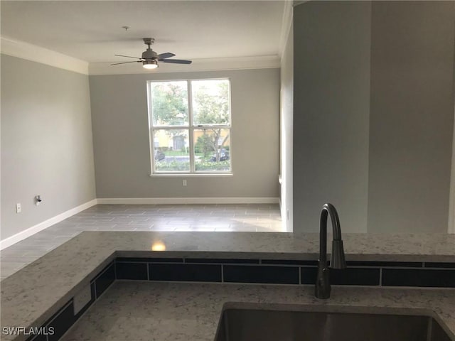 kitchen featuring ceiling fan, stone counters, ornamental molding, a sink, and baseboards