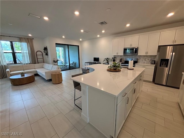 kitchen featuring white cabinets, visible vents, stainless steel appliances, open floor plan, and decorative backsplash