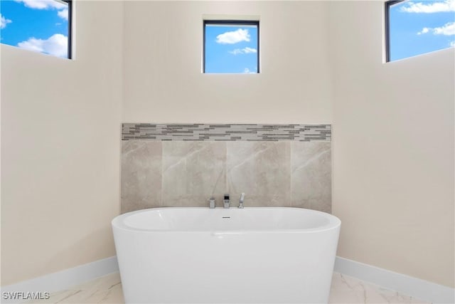 full bathroom featuring a freestanding tub, marble finish floor, baseboards, and tile walls