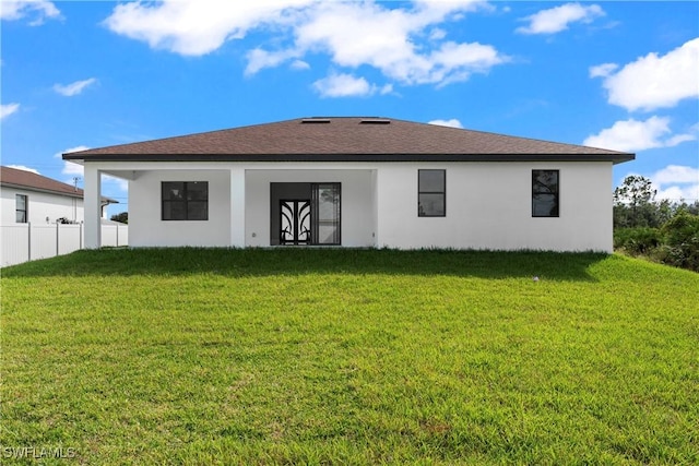 rear view of house featuring stucco siding, fence, and a lawn