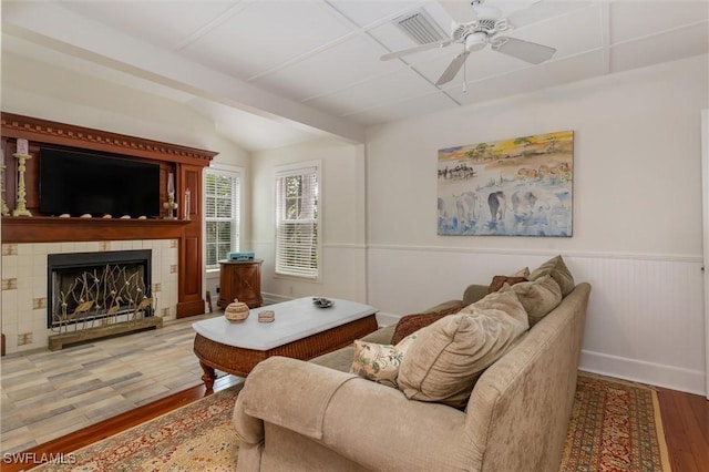 living room featuring light wood-style flooring, wainscoting, vaulted ceiling, a ceiling fan, and a tile fireplace