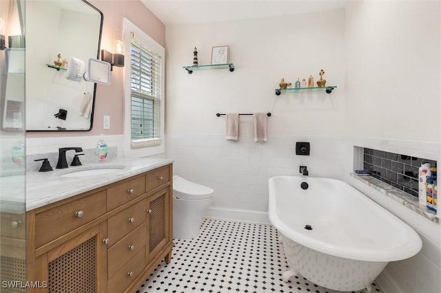 bathroom featuring a wainscoted wall, a freestanding bath, toilet, tile walls, and vanity