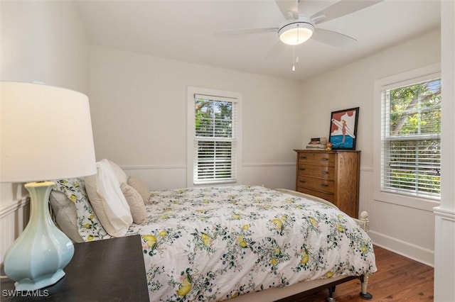 bedroom with wainscoting, a ceiling fan, multiple windows, and wood finished floors
