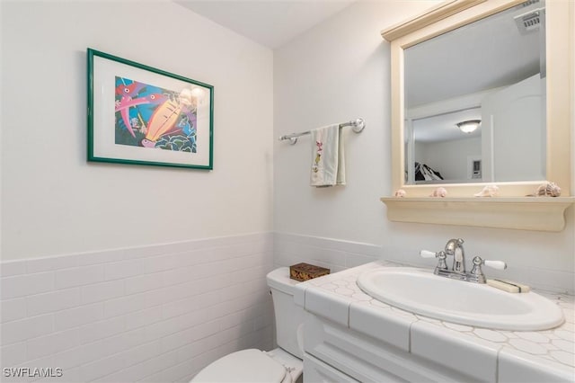 bathroom with vanity, tile walls, a wainscoted wall, toilet, and visible vents