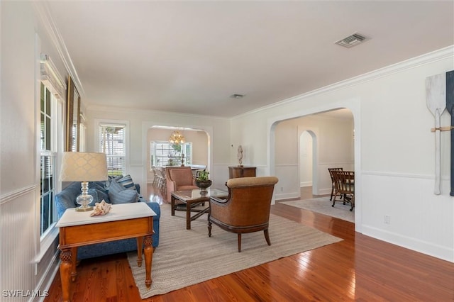 living room with wood finished floors, visible vents, arched walkways, and ornamental molding