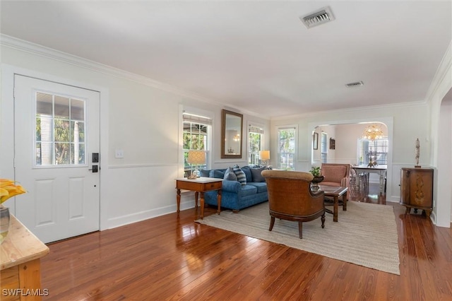 living room with wood finished floors, visible vents, crown molding, and a notable chandelier