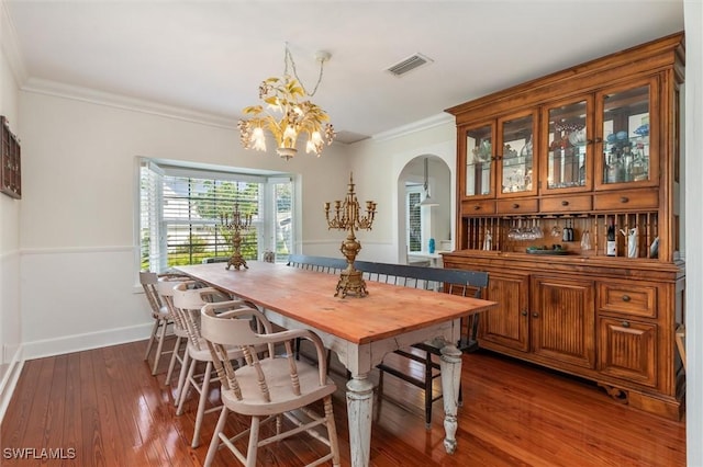 dining room with a chandelier, arched walkways, wood-type flooring, ornamental molding, and visible vents