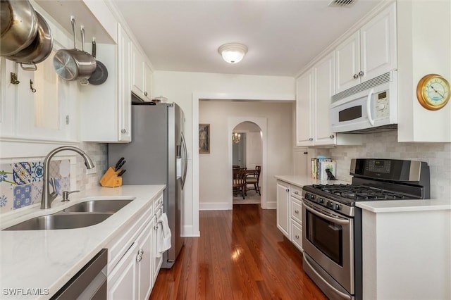 kitchen with stainless steel appliances, a sink, arched walkways, baseboards, and white cabinetry