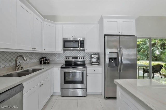 kitchen with white cabinets, a sink, appliances with stainless steel finishes, decorative backsplash, and light tile patterned flooring