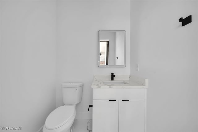 half bath featuring toilet, vanity, and baseboards