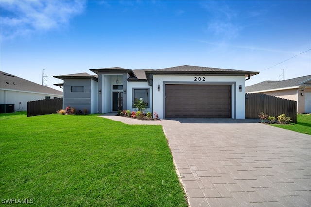 prairie-style home with an attached garage, fence, a front lawn, and decorative driveway
