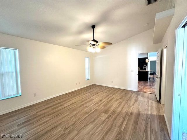 spare room with a ceiling fan, visible vents, wood finished floors, lofted ceiling, and baseboards