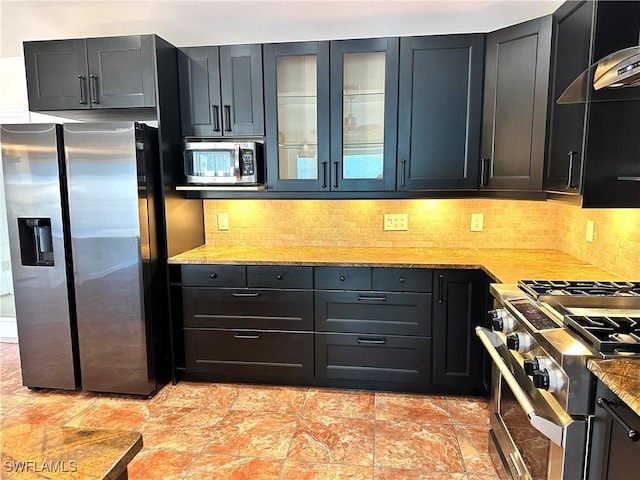 kitchen with appliances with stainless steel finishes, decorative backsplash, glass insert cabinets, and light stone countertops
