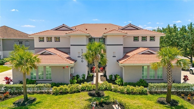 mediterranean / spanish home with a tiled roof, a front yard, and stucco siding