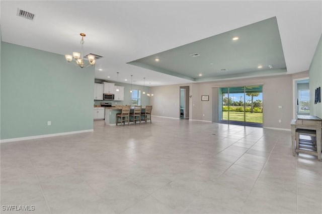 unfurnished living room with visible vents, baseboards, a notable chandelier, a tray ceiling, and recessed lighting