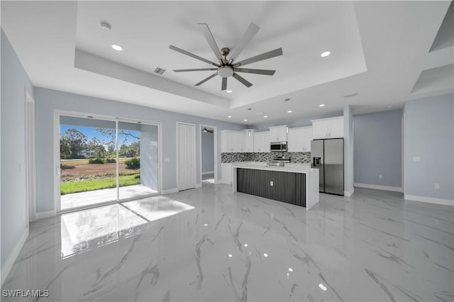 kitchen with tasteful backsplash, baseboards, ceiling fan, a tray ceiling, and stainless steel appliances