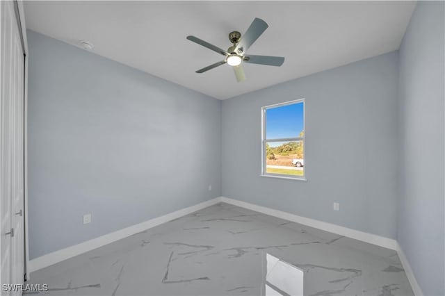 empty room with ceiling fan, marble finish floor, and baseboards
