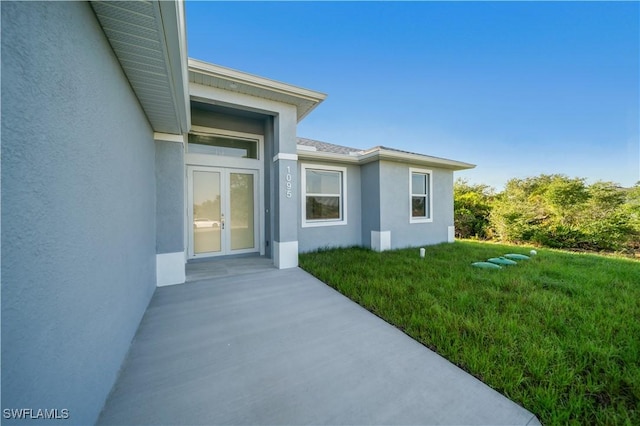 view of exterior entry featuring french doors, stucco siding, and a yard
