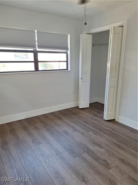 unfurnished bedroom featuring dark wood-type flooring, a closet, and baseboards