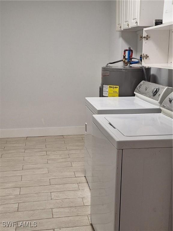 clothes washing area with baseboards, light wood-style floors, independent washer and dryer, water heater, and cabinet space