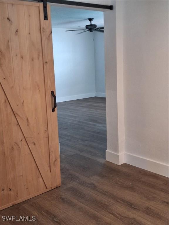 hallway featuring a barn door, dark wood-style flooring, and baseboards