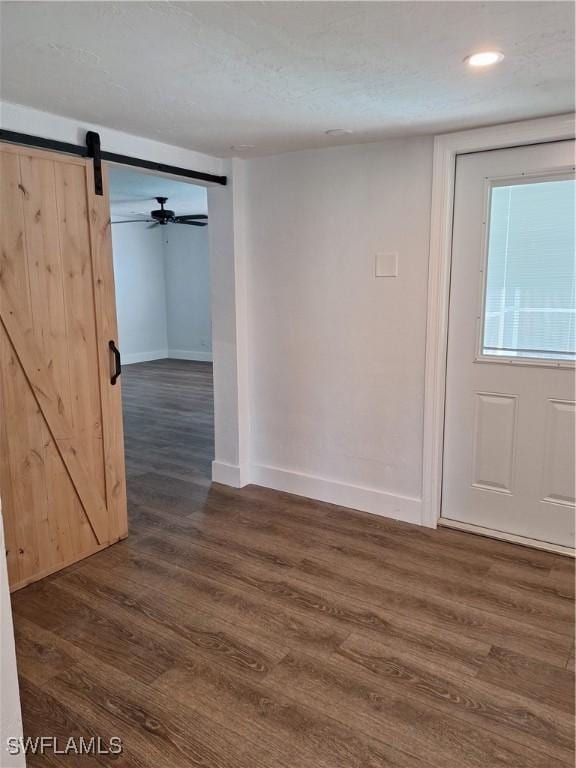 empty room featuring recessed lighting, baseboards, dark wood finished floors, and a barn door