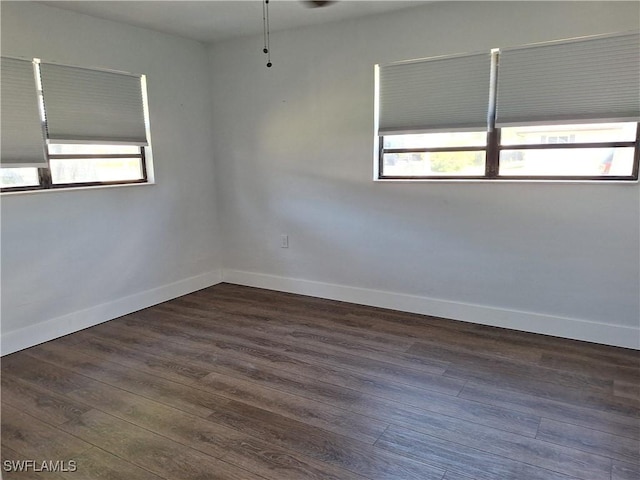 spare room featuring dark wood-style flooring, a wealth of natural light, and baseboards