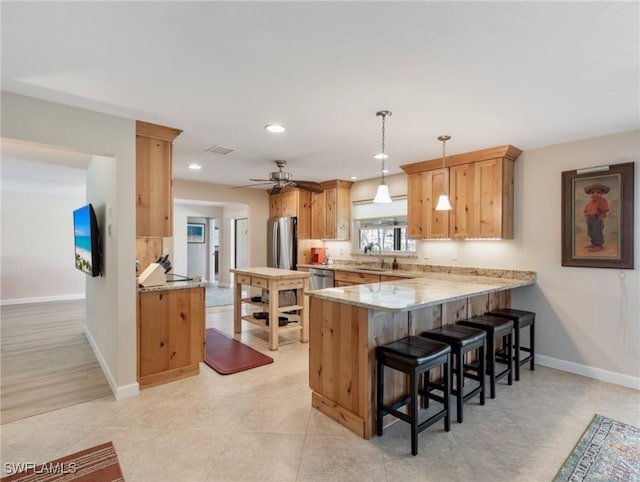 kitchen with baseboards, a peninsula, freestanding refrigerator, a breakfast bar area, and a sink