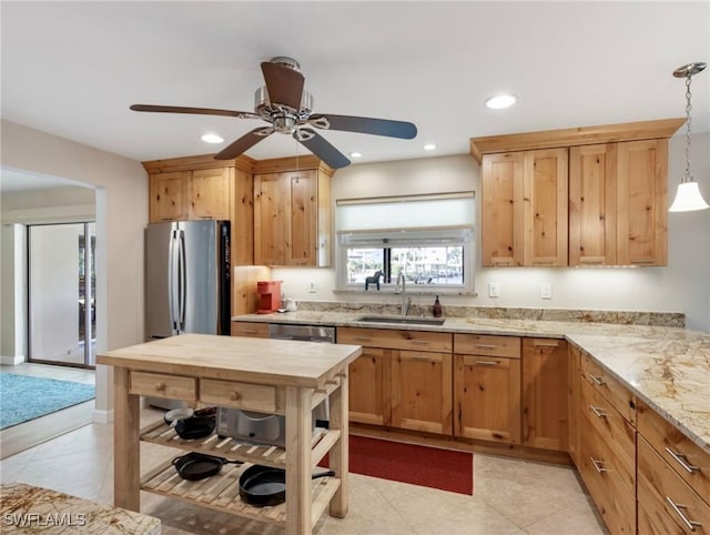 kitchen with light stone counters, freestanding refrigerator, a ceiling fan, decorative light fixtures, and a sink