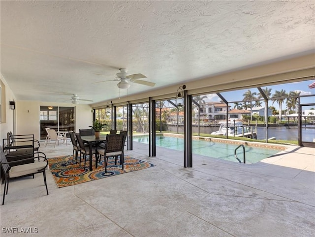 exterior space with outdoor dining space, a patio, a ceiling fan, a water view, and glass enclosure