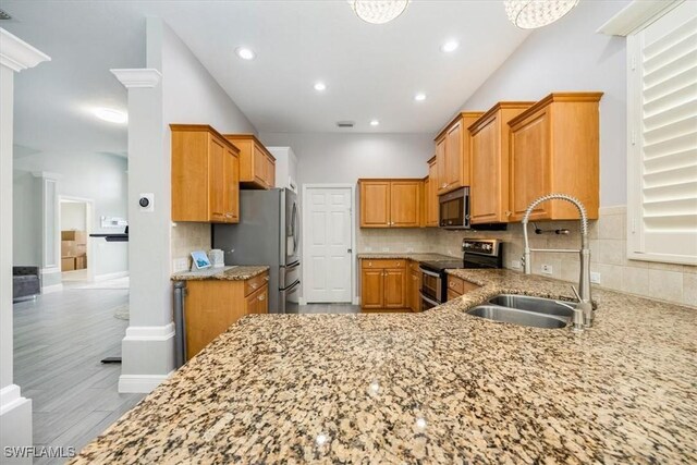 kitchen with decorative backsplash, a sink, light stone counters, and appliances with stainless steel finishes
