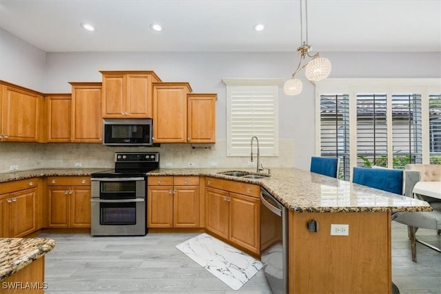 kitchen with a breakfast bar, a peninsula, light stone countertops, stainless steel appliances, and a sink