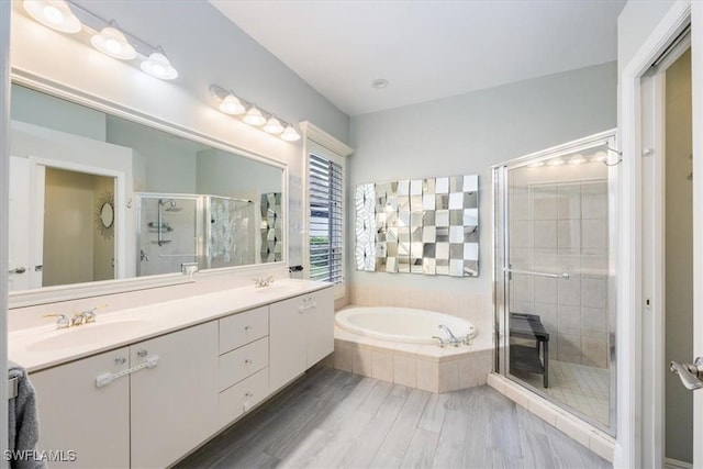 bathroom with a shower stall, a bath, wood finished floors, a sink, and double vanity