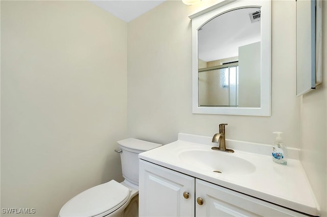 bathroom featuring toilet, visible vents, a shower with shower door, and vanity
