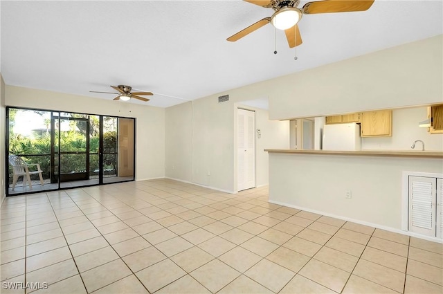 unfurnished living room with ceiling fan, visible vents, a sink, baseboards, and light tile patterned flooring