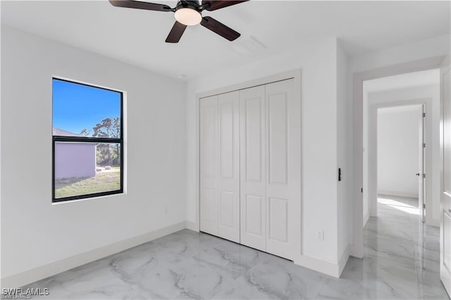 unfurnished bedroom with a closet, marble finish floor, baseboards, and a ceiling fan